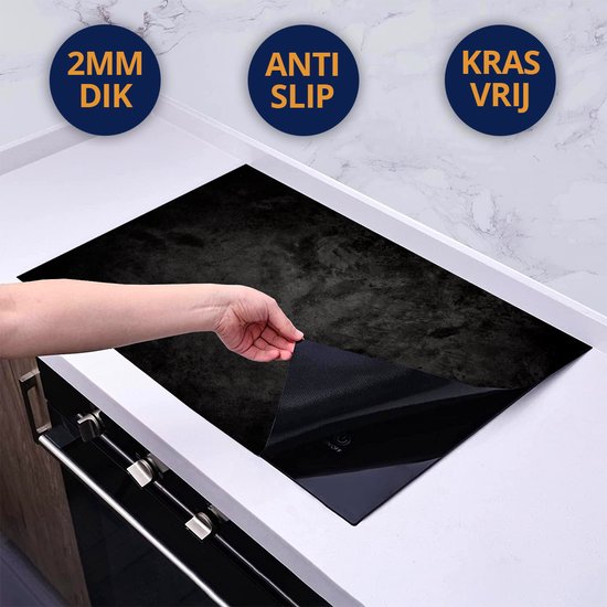 Hand plaatst een zwarte inductiebeschermer met betonlook op een glazen kookplaat.