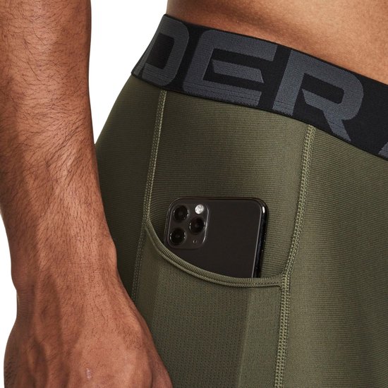 Close-up van een olijfgroene sportlegging met zijzak waarin een zwarte smartphone zit.