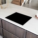 Zwarte inductiebeschermer op een wit marmeren aanrechtblad in een keuken.