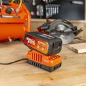 Oranje Dual Power accu op oranje lader op een houten werkbank, met luchtcompressor en cirkelzaag.