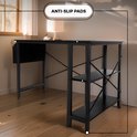 Zwart L-vormig bureau met een metalen frame en anti-slip voetjes, in een woonkamer setting.
