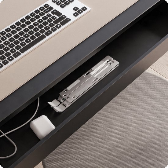 Opgevouwen zilverkleurige laptopstandaard van Voomy in een bureaulade, naast een oplader en toetsenbord.