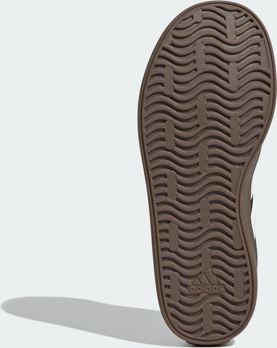 Bruine buitenzool van een zwarte kindersneaker van adidas met golvend profiel.