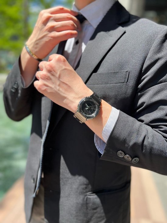 Man in zwart pak met gestreepte overhemd, strikt das en draagt een zwart G-SHOCK horloge.