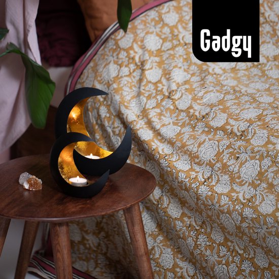 Bougeoirs lune noirs à l'intérieur doré, sur une table d'appoint en bois à côté d'un lit à imprimé floral.