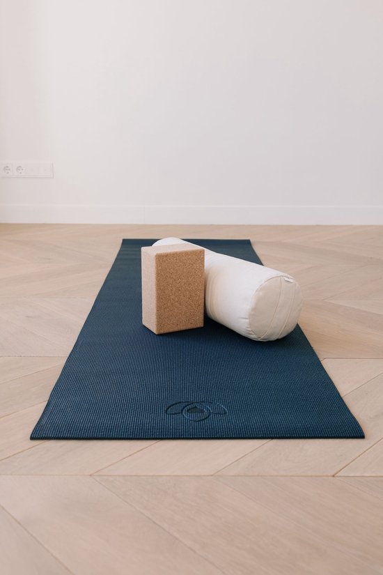 Donkerblauwe yogamat met ribbelpatroon, met daarop een bruine yogablok van kurk en een wit nekkussen.
