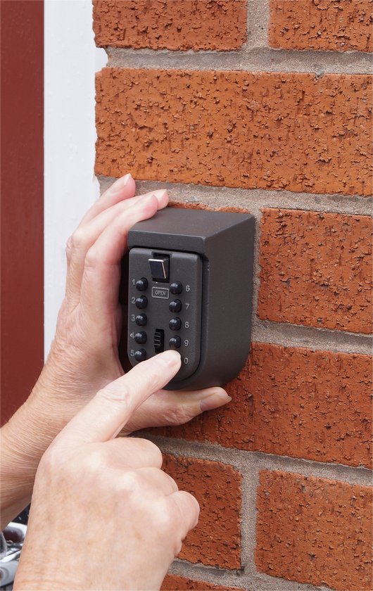 Handen die een zwarte metalen sleutelkluis op een bakstenen muur bedienen. Cijfer 9 wordt ingedrukt.