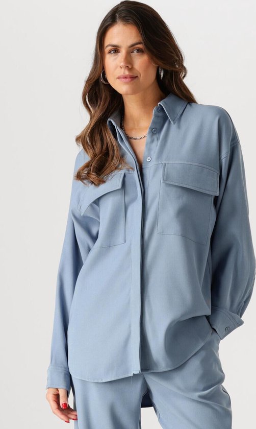 Blauwe oversized blouse met twee borstzakken en kraag, gedragen door een model.