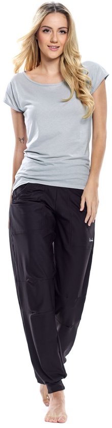 Model in een zwarte, nauwsluitende joggingbroek en een lichtgrijs T-shirt, staand met de handen in de zakken.