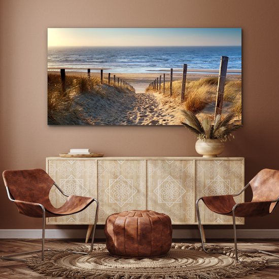 Un sentier à travers les dunes, bordé d'herbes, mène à la mer au coucher du soleil.