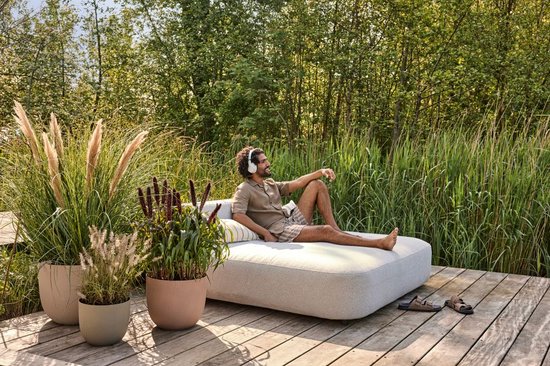 Man zit op loungeset op houten dek, met twee bloempotten met gras op de voorgrond.