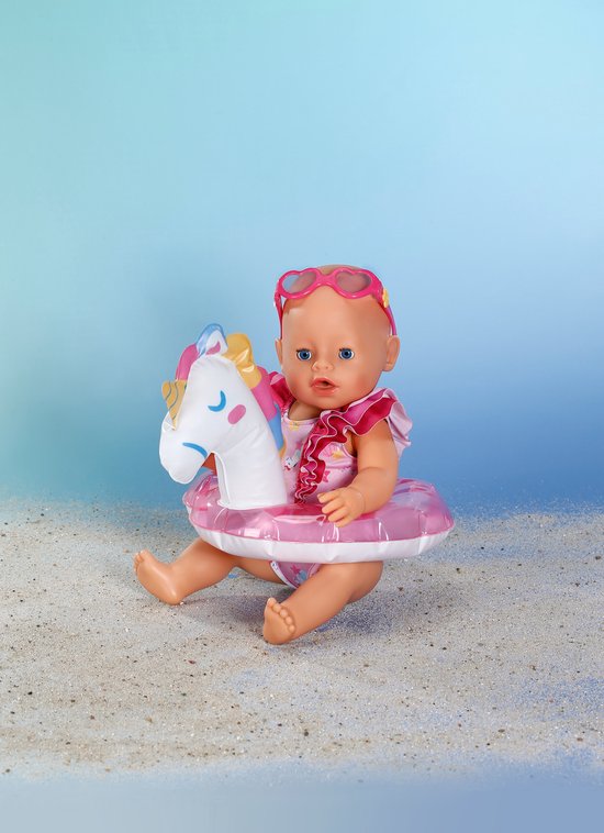 Zittende baby pop met hartjes zonnebril, glitter zwemband met eenhoorn en een glitter zwempak.