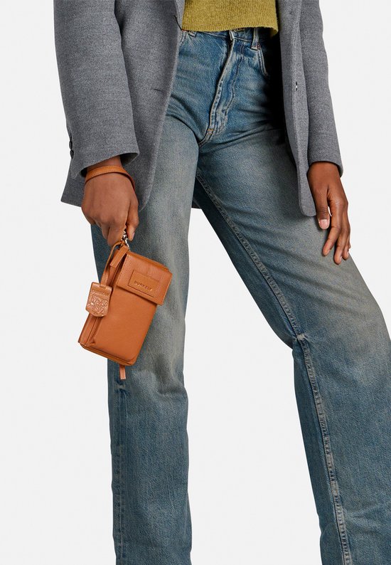 Model met cognac gekleurde telefoonportemonnee in de hand, met spijkerbroek en blazer.