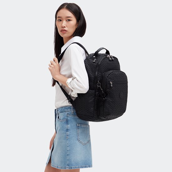 Vrouw met zwarte Kipling rugzak met patroon, wit overhemd en spijkerrok.