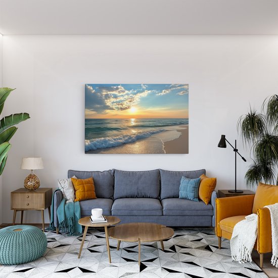 Canvas schilderij van zonsondergang aan zee, boven een grijze bank met gele en blauwe kussens.
