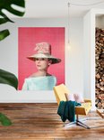 Audrey Hepburn portant un grand chapeau de paille et un nœud rose sur fond rose.