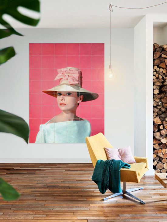 Audrey Hepburn portant un grand chapeau de paille et un nœud rose sur fond rose.