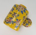 Gele pot met deksel, versierd met roze bloemen, blauwe bladeren en een vlinder.