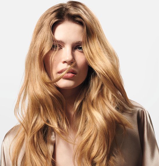 Close-up portret van een vrouw met lang, golvend, lichtblond haar dat zachtjes door de wind wordt geblazen, met een glanzende satijnen outfit.