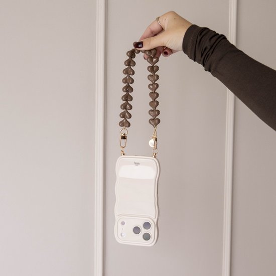 Bruine hartjeskoord bevestigd aan een off-white golvend telefoonhoesje, vastgehouden door een hand met donkere nagellak.