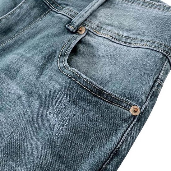Blauwe jeans met lomp, rafelige detail en koperkleurige knoop bij de zak.