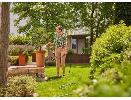 Vrouw met bloemenblouse en een roze broek besproeit een boom in een tuin met Gardena Liano Life slang.