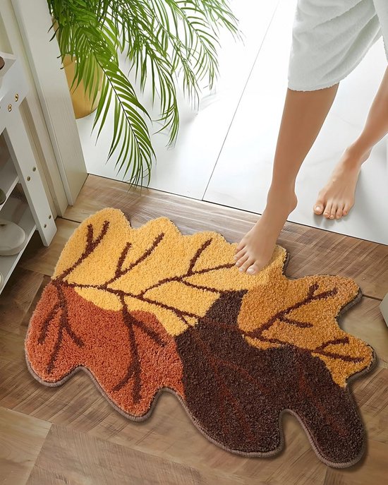 Voet stapt op een bruine en oranje herfstblaadjes badmat bij een deur, met planten.