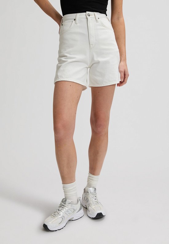 Model in crèmekleurige Lee-shorts met wijde pijpen en witte sneakers.
