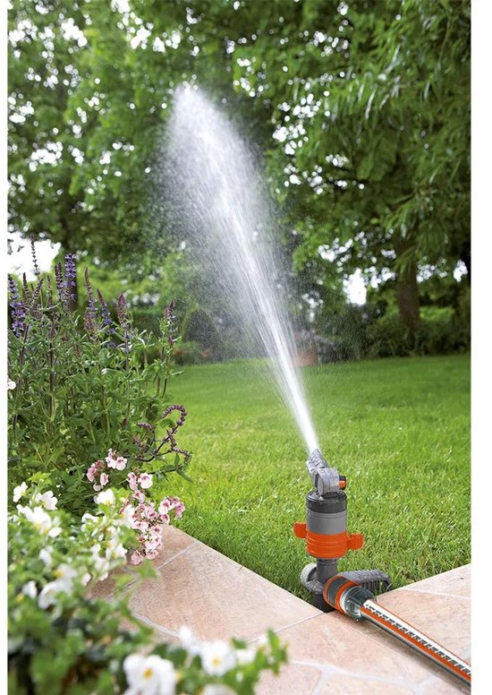 GARDENA turbinesproeier in gebruik, sproeit water op een groen gazon naast bloemen