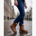Meisje met spijkerbroek en bruine biker boots met bontkraag, staand op straat.