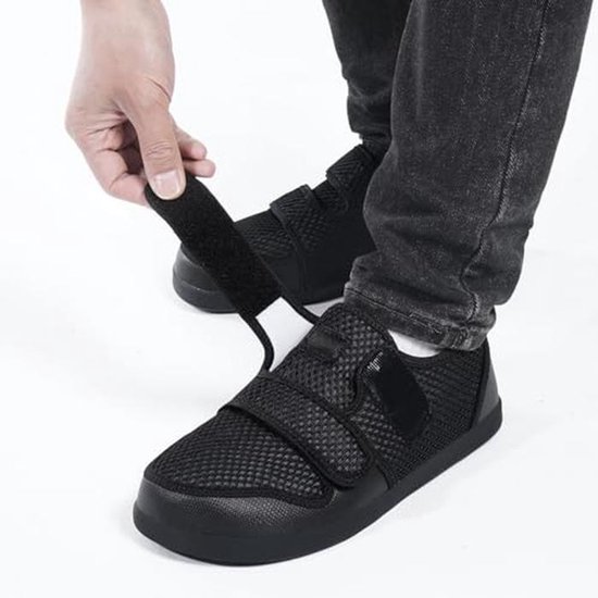 Voet van een persoon die een zwarte ademende mesh schoen met klittenbandsluiting aantrekt.