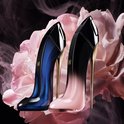 Twee pump-vormige parfumflessen: één in donkerblauw en één in roze, beide met gouden hakken, op de achtergrond van grote roze bloemen.