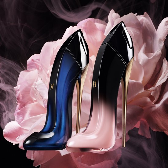 Twee pump-vormige parfumflessen: één in donkerblauw en één in roze, beide met gouden hakken, op de achtergrond van grote roze bloemen.