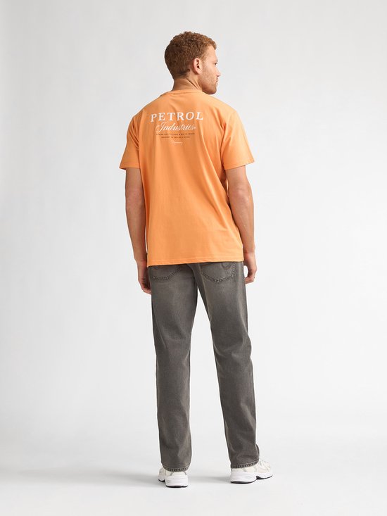 Man van achteren draagt een oranje t-shirt met "PETROL Industries" op de rug en een grijze jeans.