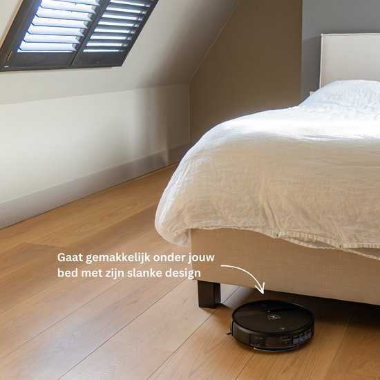Zwarte robotstofzuiger onder een bed met witte lakens, met tekst "Gaat gemakkelijk onder jouw bed met zijn slanke design".