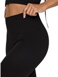 Detail van een zwarte, nauwsluitende sportlegging met hoge taille en geribd patroon. Model trekt de tailleband omhoog.