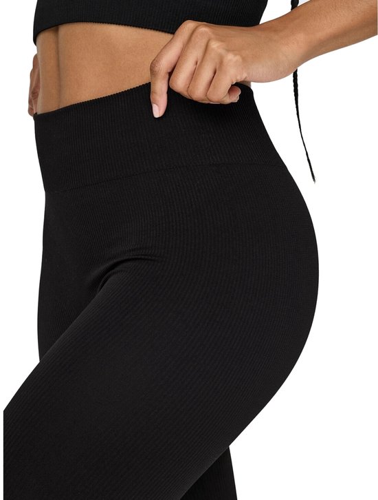 Detail van een zwarte, nauwsluitende sportlegging met hoge taille en geribd patroon. Model trekt de tailleband omhoog.