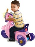 Jongen zit op roze VTech driewieler loopscooter met paarse details en knipperende lampjes.
