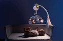 Baby in een wiegje kijkt omhoog naar een blauwe muziekmobiel met een lachende maan.