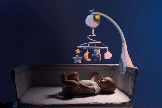 Baby in een wiegje kijkt omhoog naar een blauwe muziekmobiel met een lachende maan.