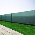Een schutting bedekt met groen schaduwdoek, met een rechte tegelpad en gras ernaast.