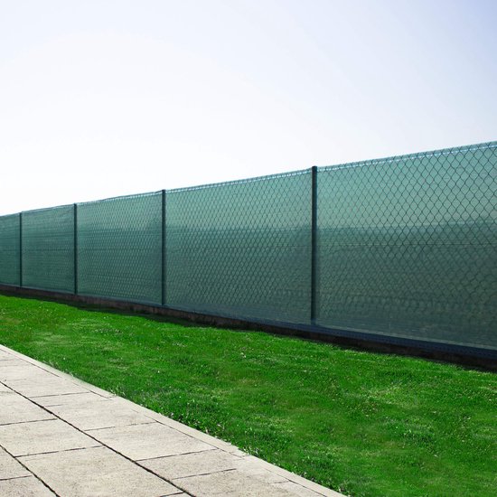 Een schutting bedekt met groen schaduwdoek, met een rechte tegelpad en gras ernaast.