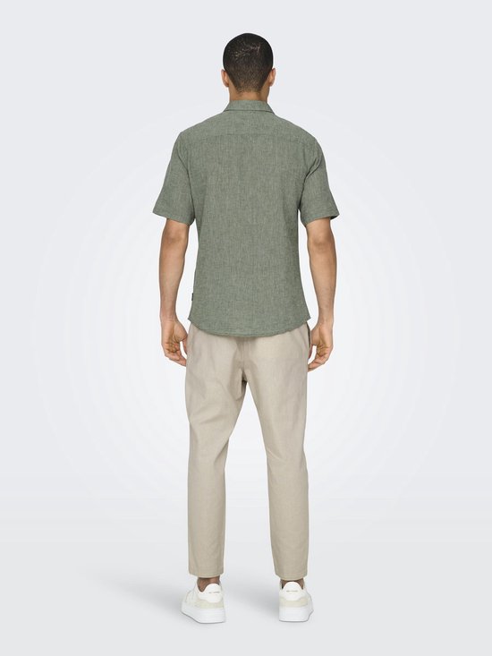 Zicht op de achterkant van een man die een lichtgroen linnenmix overhemd met korte mouwen en beige broek draagt.