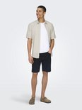 Man met een beige linnen mix overhemd met korte mouwen, een witte t-shirt en een donkerblauwe korte broek.