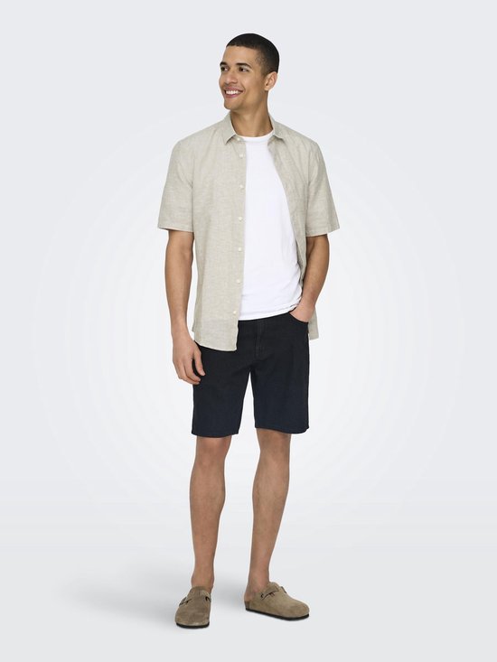 Man met een beige linnen mix overhemd met korte mouwen, een witte t-shirt en een donkerblauwe korte broek.