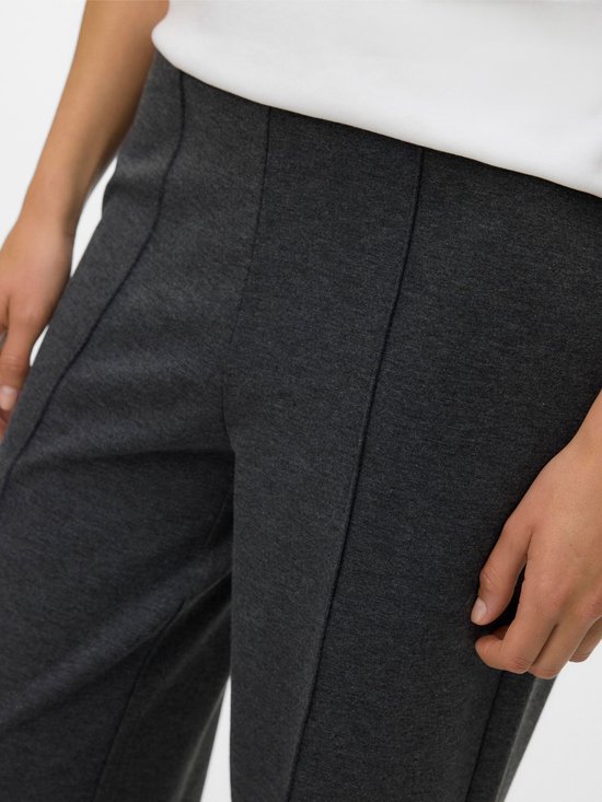 Detail van een donkergrijze broek met wijde pijpen en verticale naden, gedragen met een witte top.