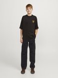 Jongen met een glimlach, draagt een zwart T-shirt met gele print en zwarte cargobroek, staand.