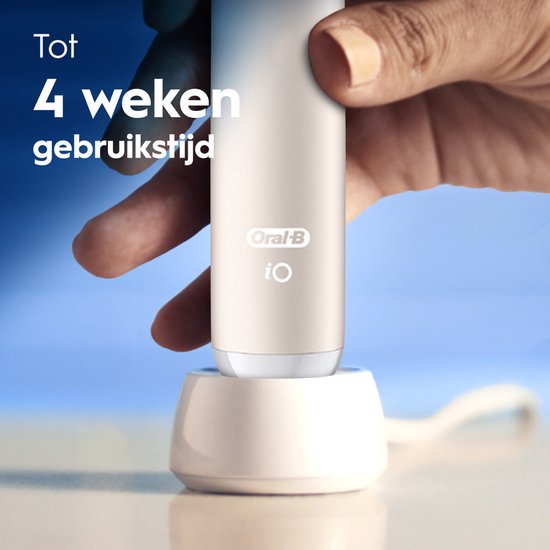 Een hand houdt de crème-kleurige Oral-B iO tandenborstel vast in een witte oplader.