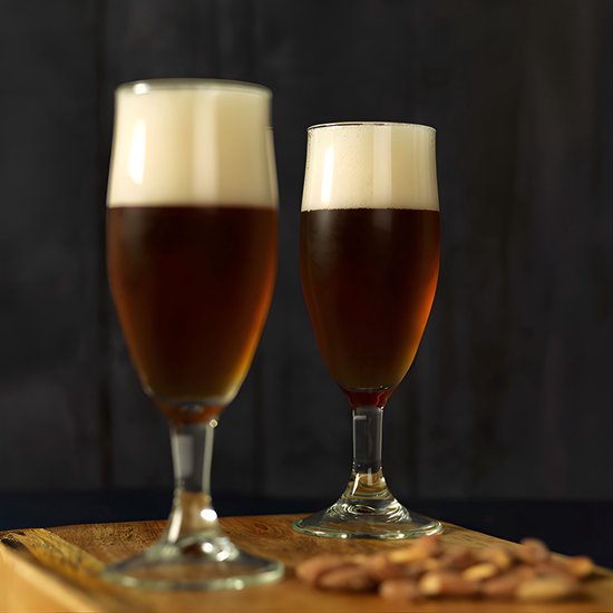 Twee glazen donker bier met schuimkoppen op een houten plank met amandelen.
