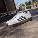 Wit leren Adidas VL Court 3.0 sneakers met bruine zool, zwarte strepen en Adidas logo, op een straat met palmbomen.